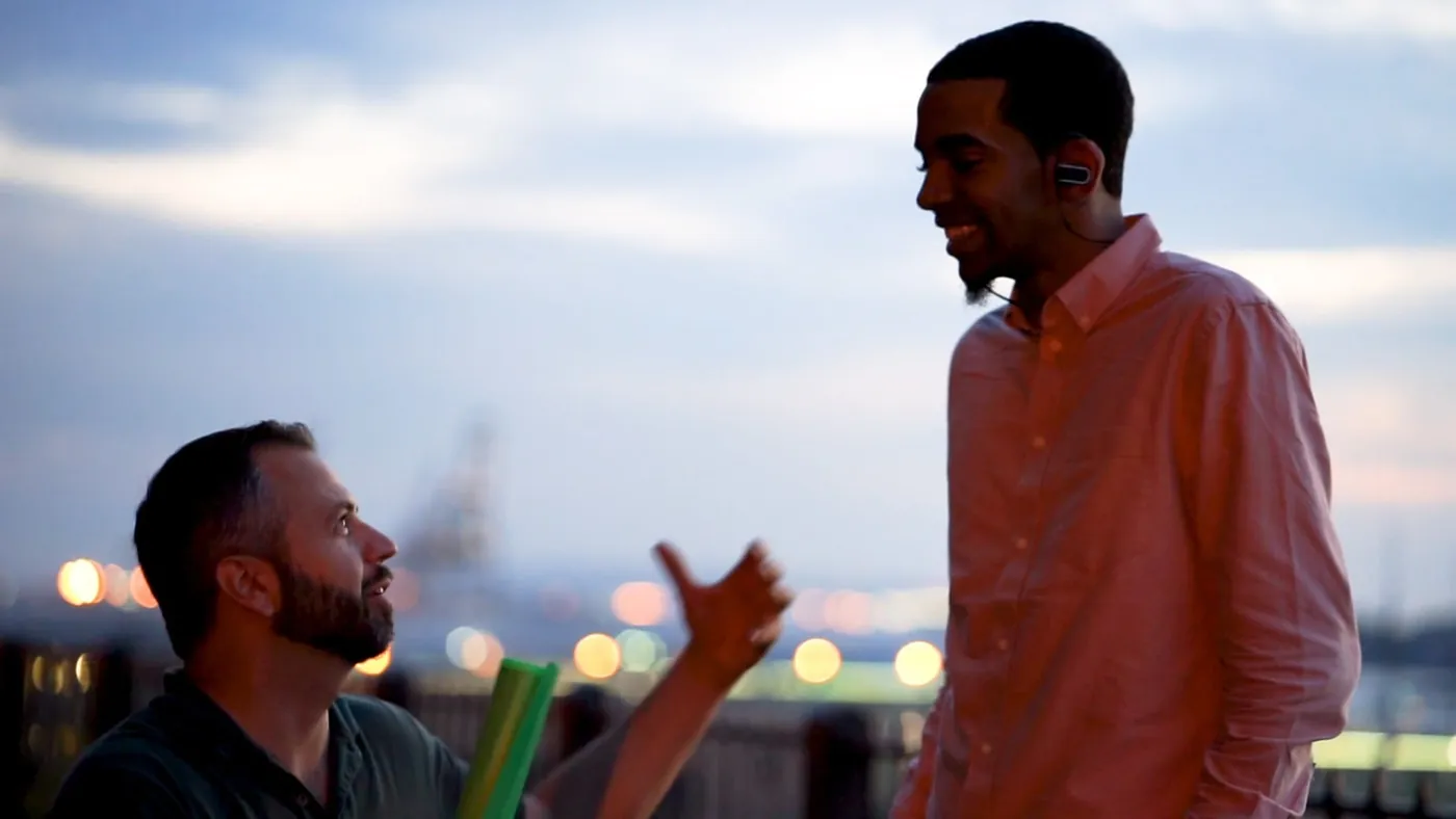 Two actors mid-conversation on a rooftop at dusk
